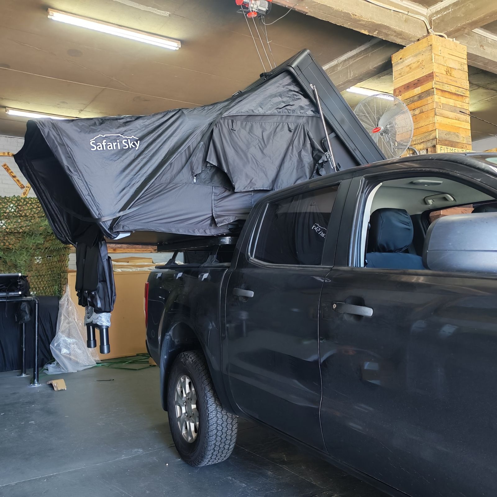 Safari Sky tent half-open on a dark double cab in the fitment bay