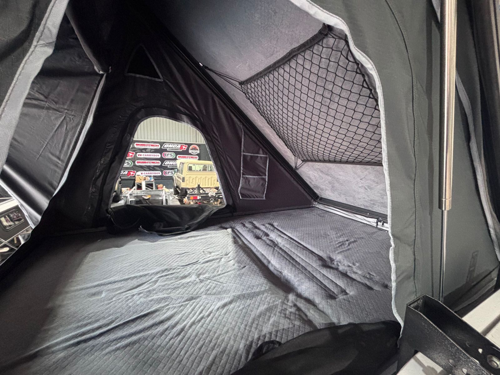 Inside a Safari Sky rooftop tent — quilted mattress, storage net and window view