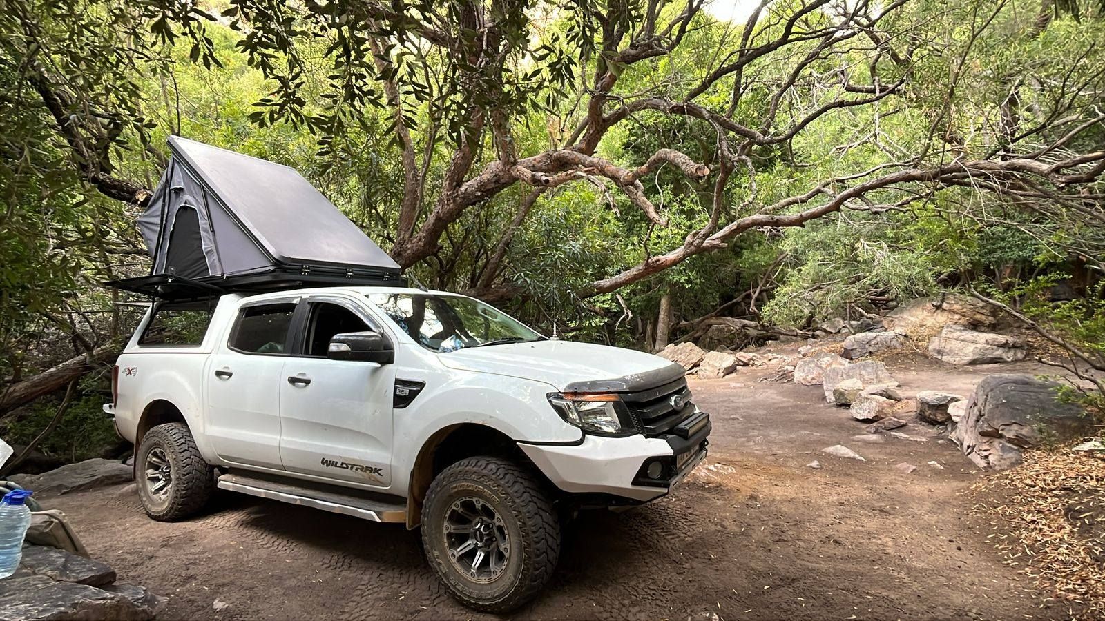 White Ford Ranger Wildtrak with an open clamshell rooftop tent in a forest clearing