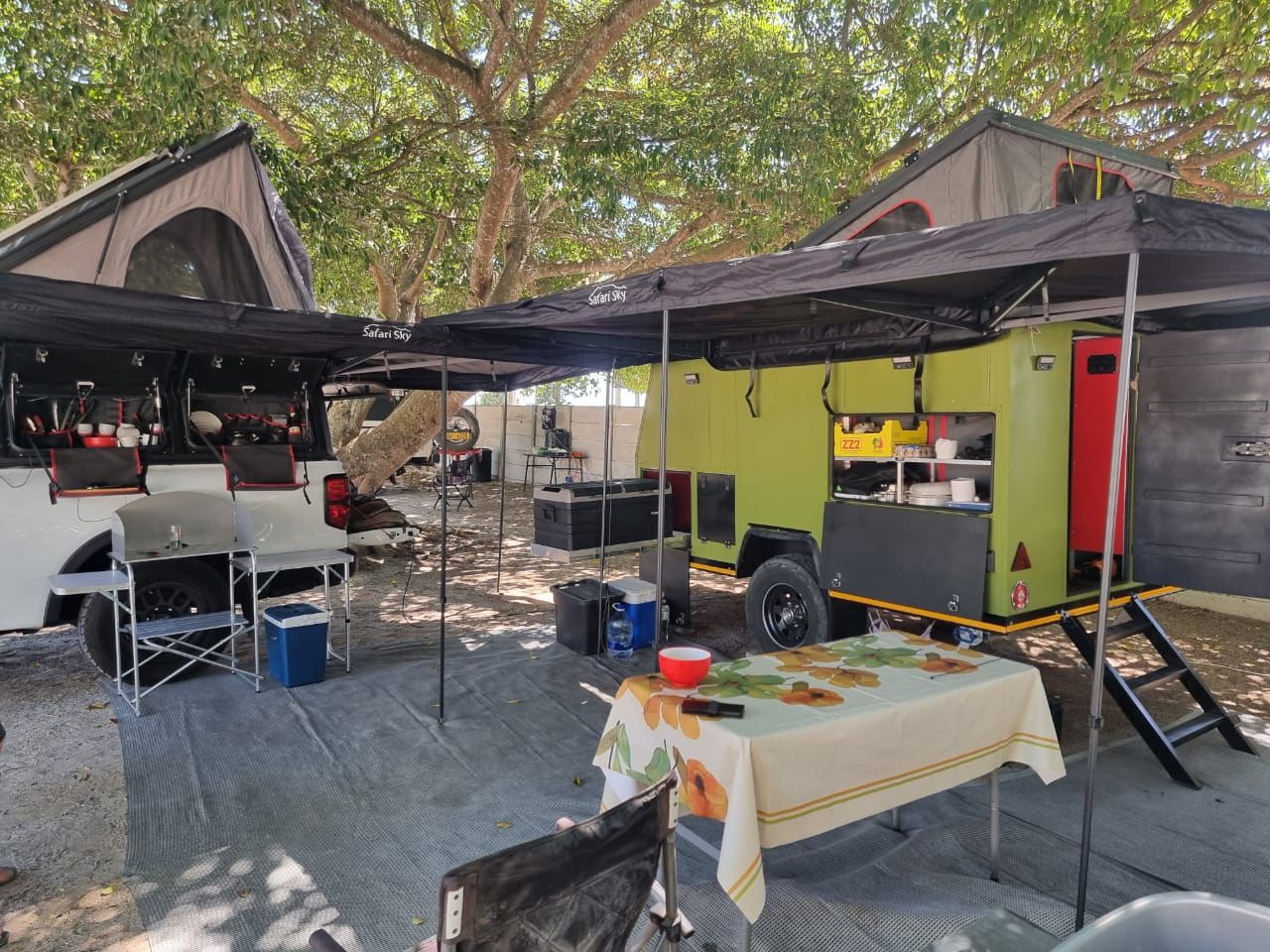 Full camp setup with Safari Sky awnings, trailer and kitchen under the trees