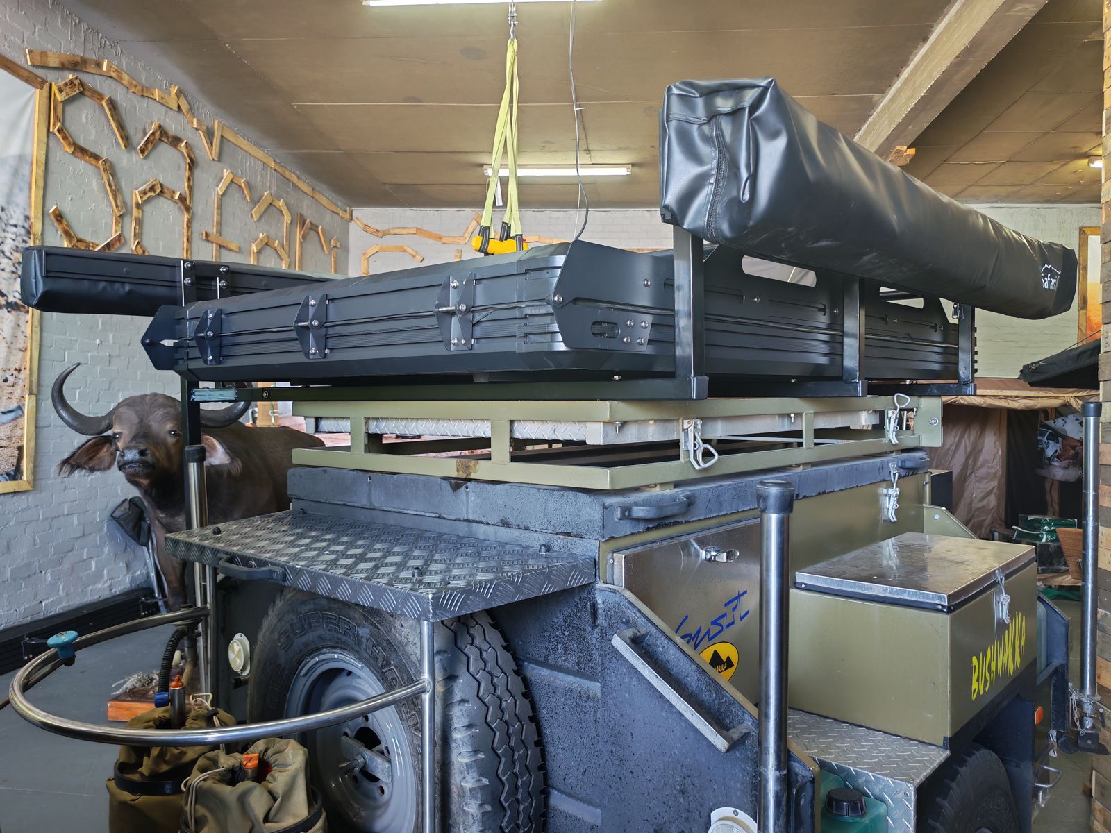 Closed rooftop tent and packed awning on an olive Bushwakka trailer in the showroom